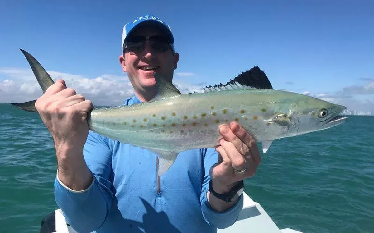 Angler with a catch on a daytime Miami fishing charter with the skyline behind - Nomad Fishing Charters